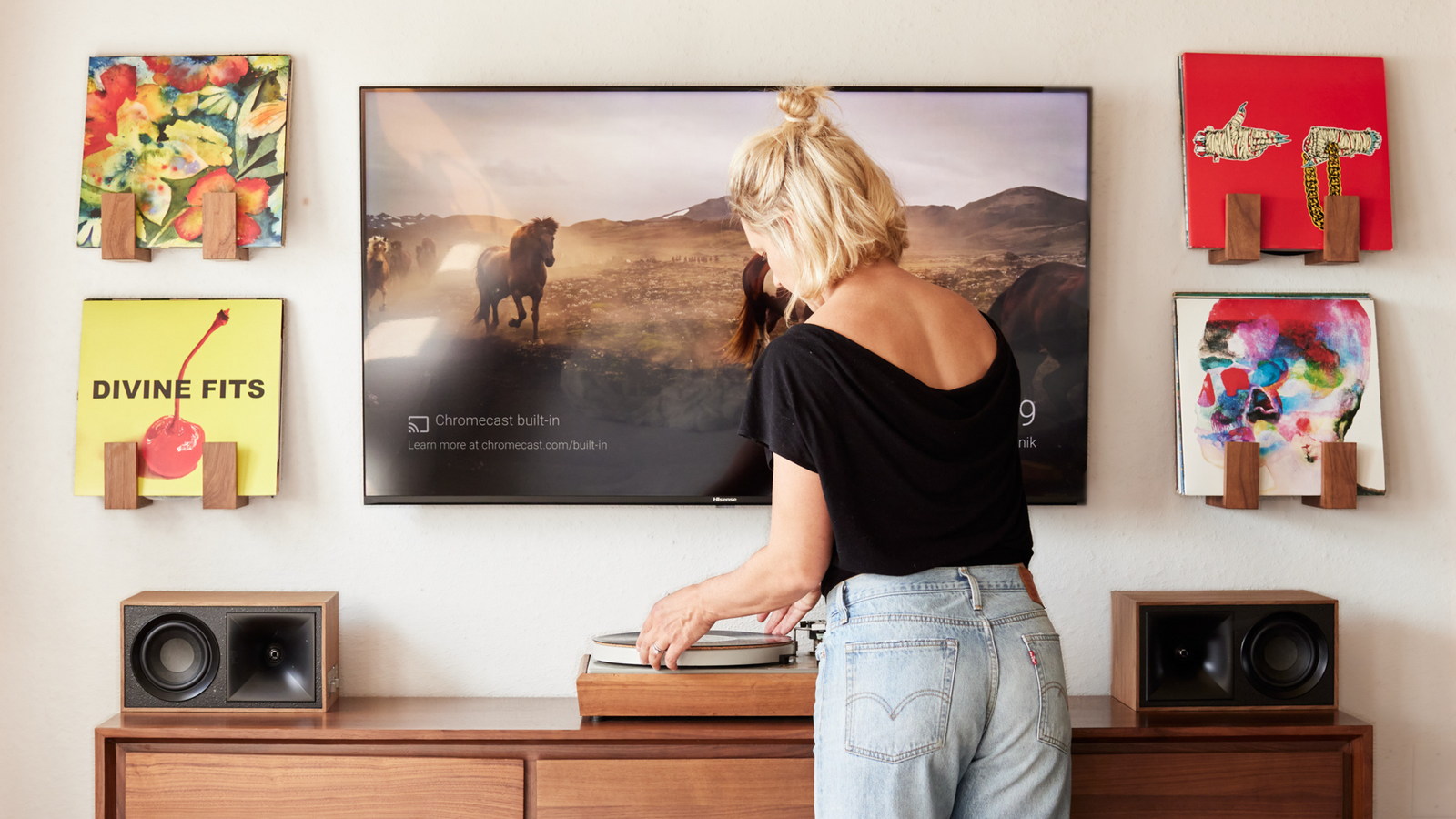 A TV with 4 wall mount record shelves mounted 2 on each side above a walnut media console with a vintage Bogen B-52 record player and Klipsch Fives powered speakers
